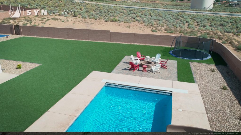 Backyard with clean artificial grass and a clear blue pool with squared edges